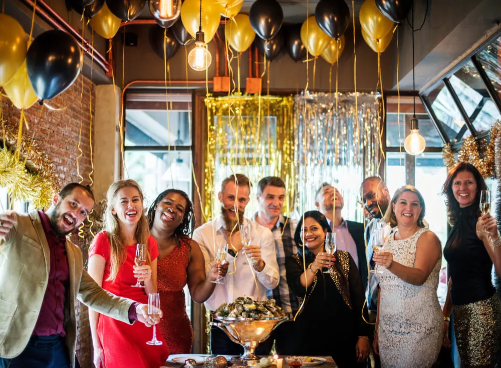 a group of people holding glasses and standing in a room with balloons